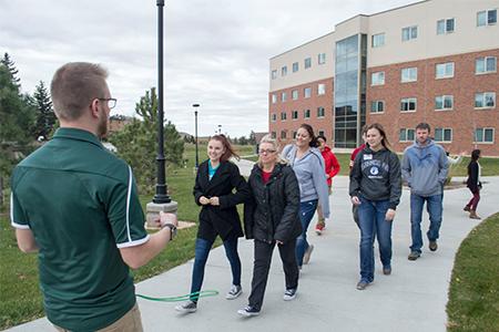 Six people are given a tour of campus by a male guide.